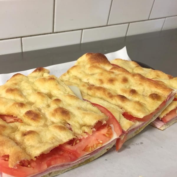 Three focaccia sandwiches with ham, cheese, and tomato slices on a white surface.