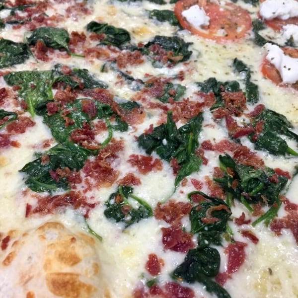 Close-up of a white pizza with spinach, bacon, sliced tomatoes, and dollops of ricotta cheese.