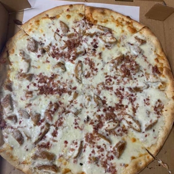 A white pizza from Pizza Village IV, topped with creamy sauce, chicken, and bacon bits.