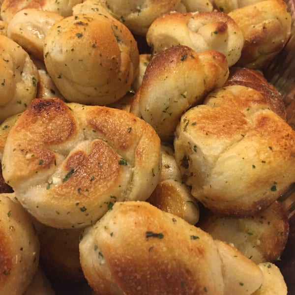 Close-up of golden-brown garlic knots, sprinkled with herbs, from Pizza Village IV.