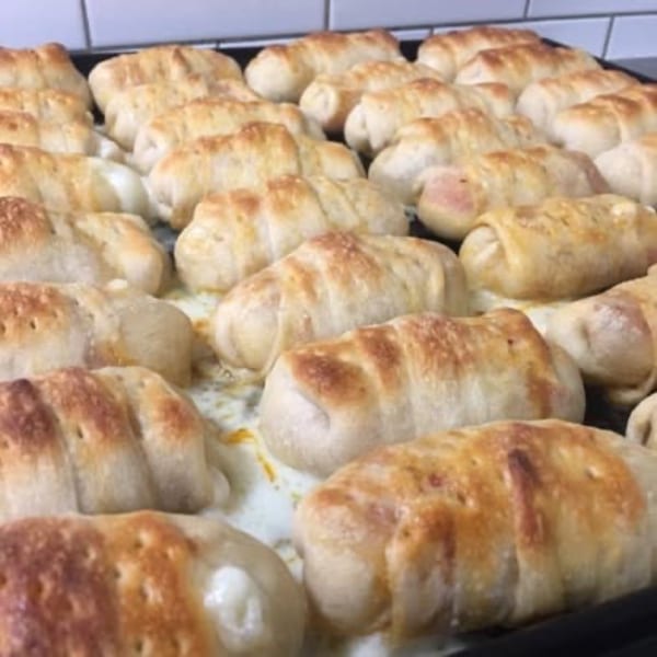 Rows of golden-brown baked pizza rolls, some with melted cheese oozing out, on a baking sheet.