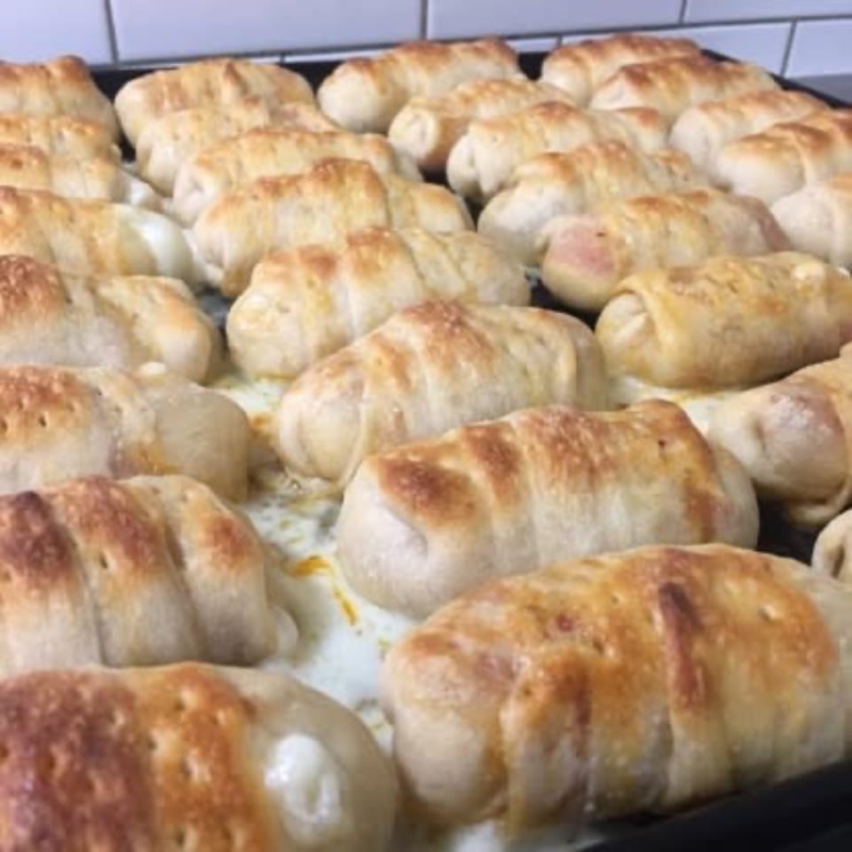 Rows of golden-brown baked pizza rolls, some with melted cheese oozing out, on a baking sheet.