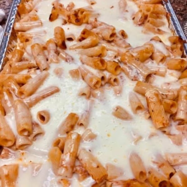 Baked ziti pasta with melted white cheese in a rectangular foil pan.