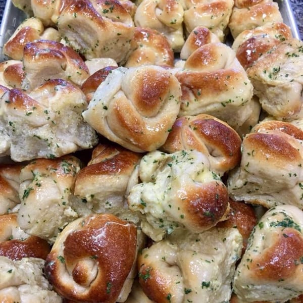 Close-up of golden-brown garlic knots with green herbs, glistening with butter or oil.