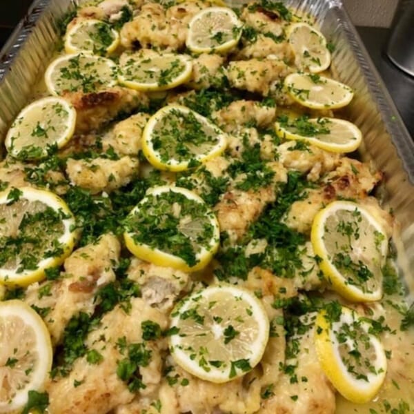 Lemon chicken with parsley in a large foil pan, ready for catering from Pizza Village IV.