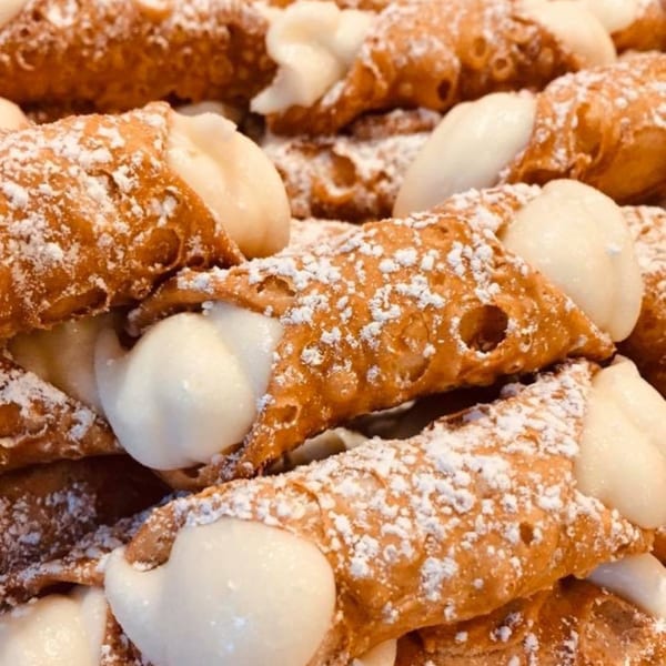 Close-up of several golden-brown cannoli filled with white cream and dusted with powdered sugar.
