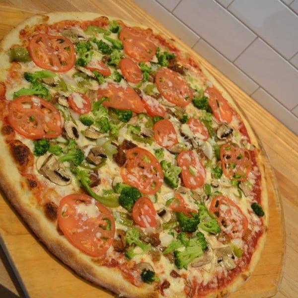 Pizza Village IV's veggie pizza with tomatoes, broccoli, mushrooms, and green peppers on a wooden peel.