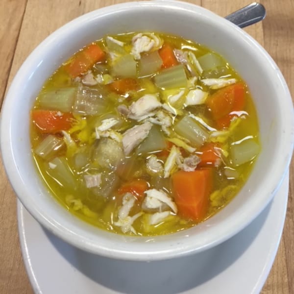A white bowl of chicken noodle soup with carrots and celery on a wooden table.