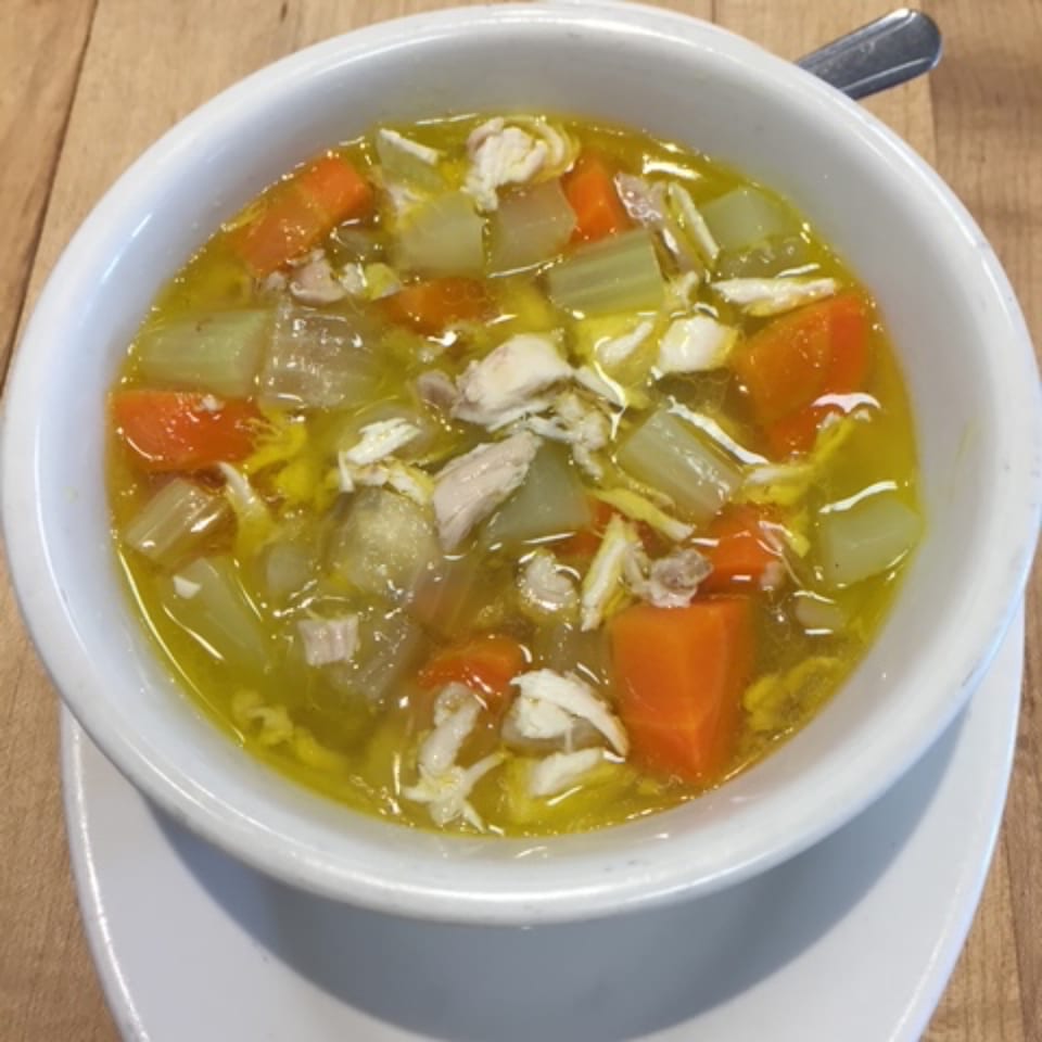 A white bowl of chicken noodle soup with carrots and celery on a wooden table.