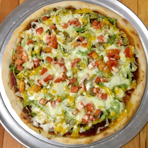 A Pizza Village IV taco pizza, topped with melted cheese, shredded lettuce, diced tomatoes, and yellow sauce.