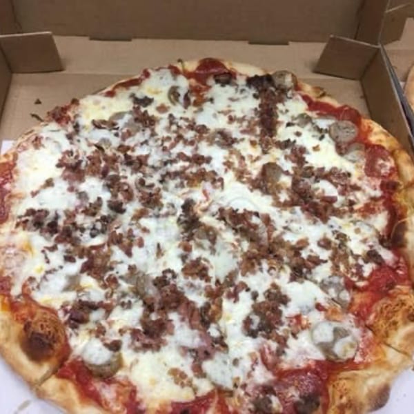 A Pizza Village IV meat lover's pizza with pepperoni, sausage, and bacon in a cardboard box.