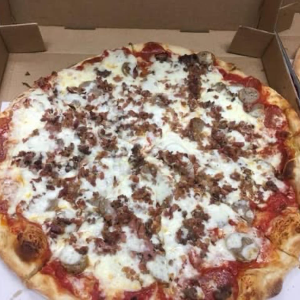 A Pizza Village IV meat lover's pizza with pepperoni, sausage, and bacon in a cardboard box.