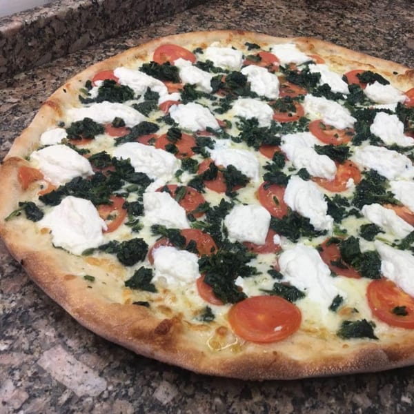 A Pizza Village IV pizza with spinach, sliced tomatoes, and dollops of ricotta cheese.